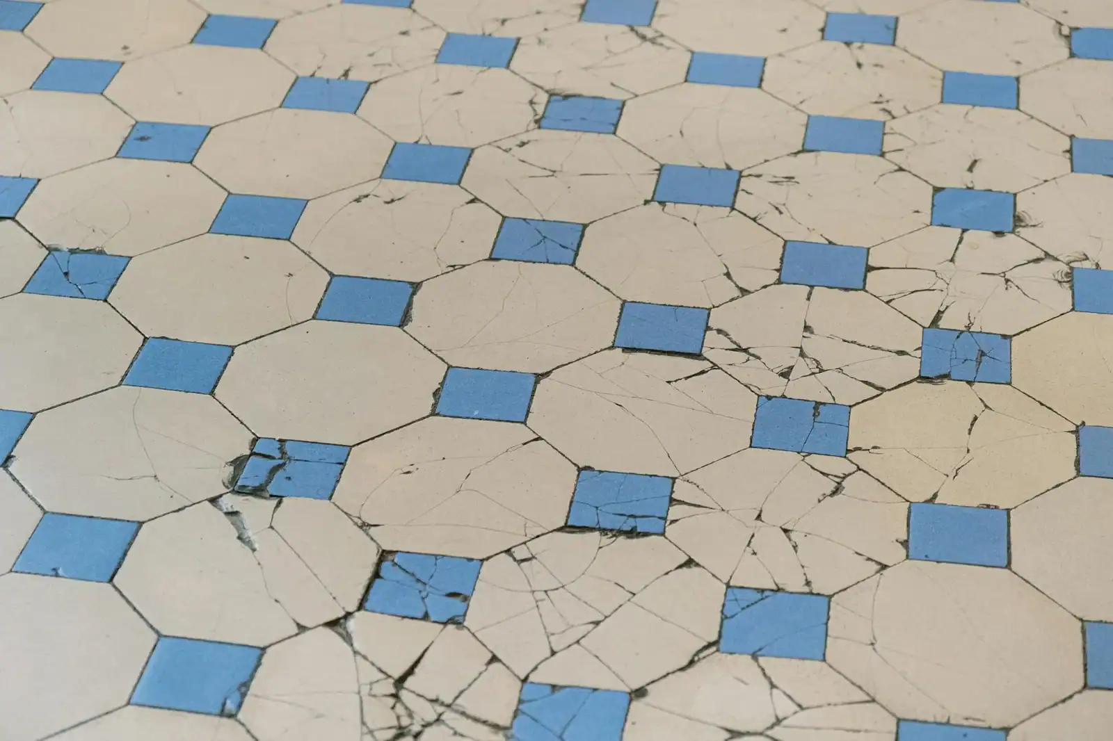 A detailed view of aged cracked tiles with a blue and white geometric pattern.