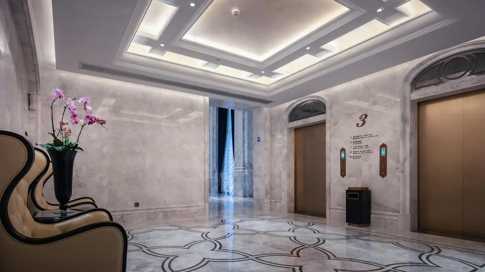 Opulent hotel lobby interior featuring marble floors and an elevator area with floral decoration.