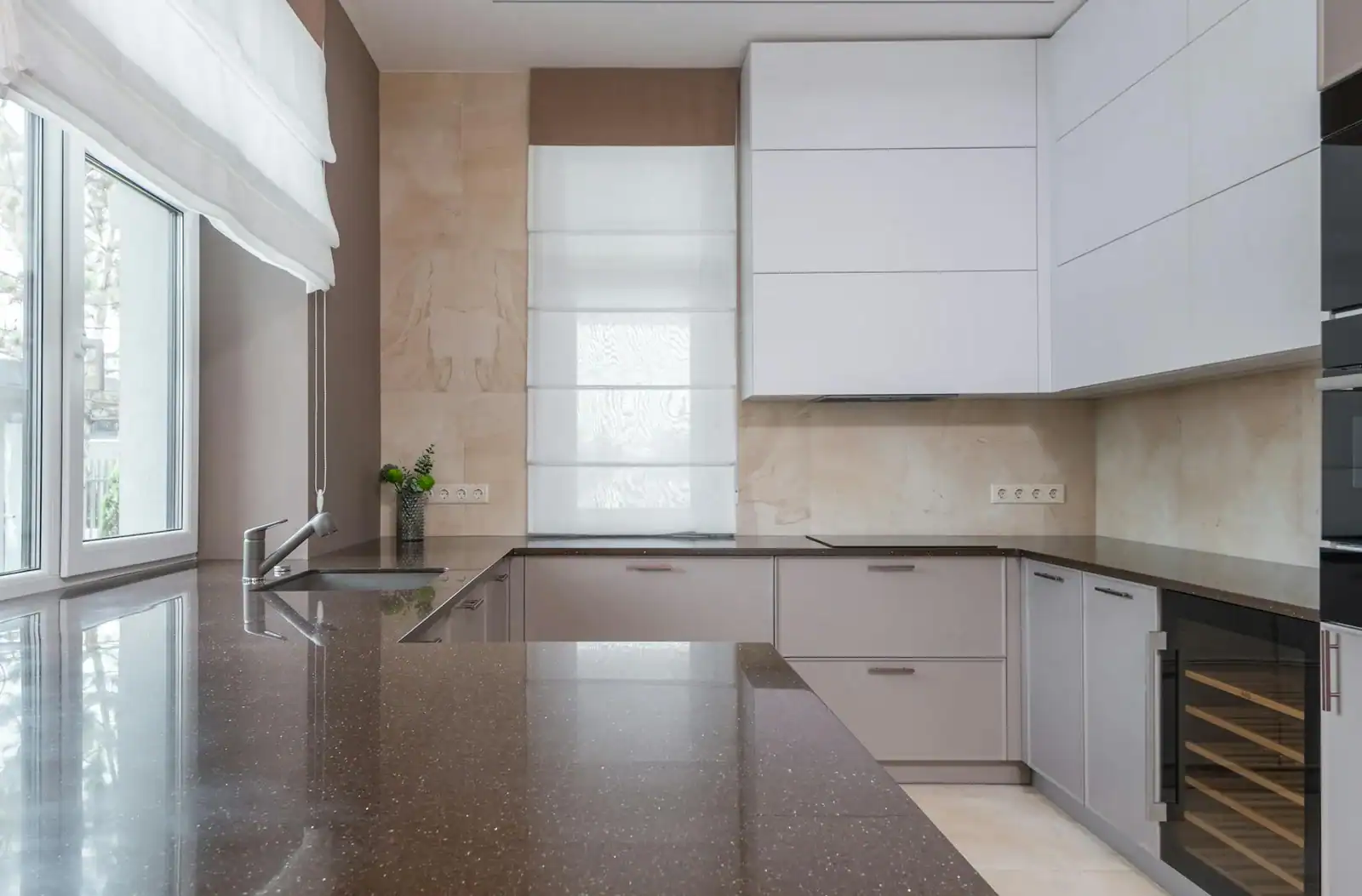 Minimalist interior kitchen design with stone countertop of marble color with sink and chrome plated faucet lying on cupboard with built in stove and electric appliances in daylight