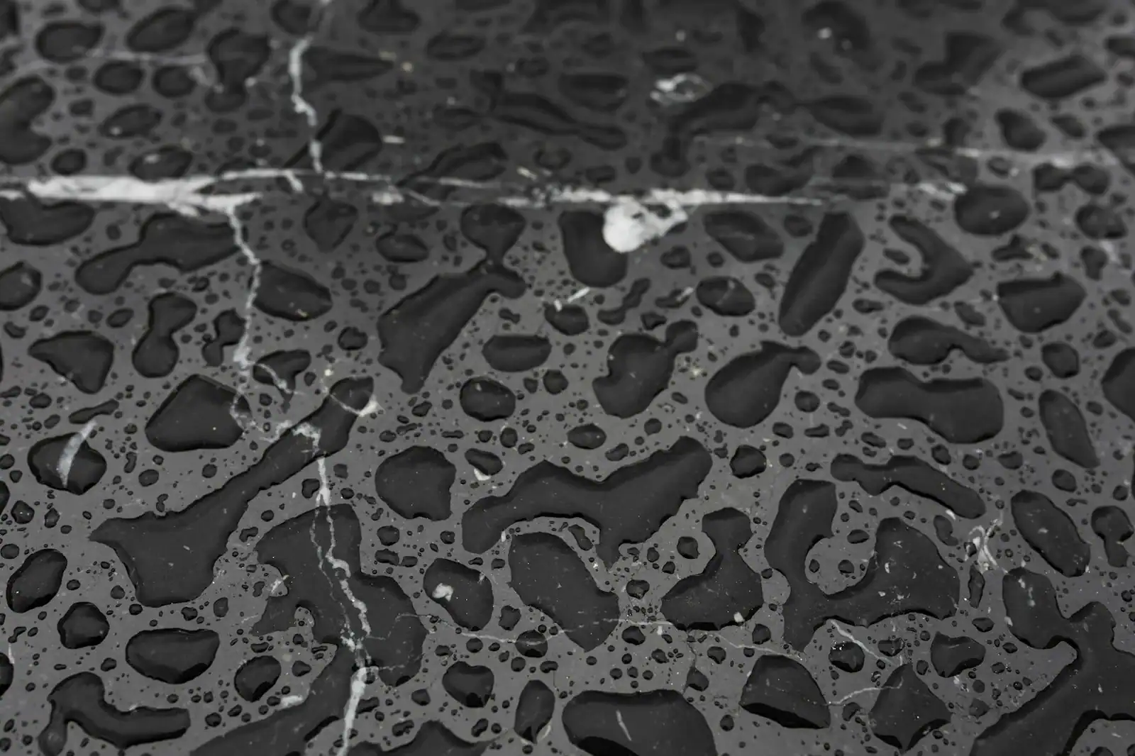 Detailed close-up photo of water droplets on a dark marble surface, highlighting texture and pattern.