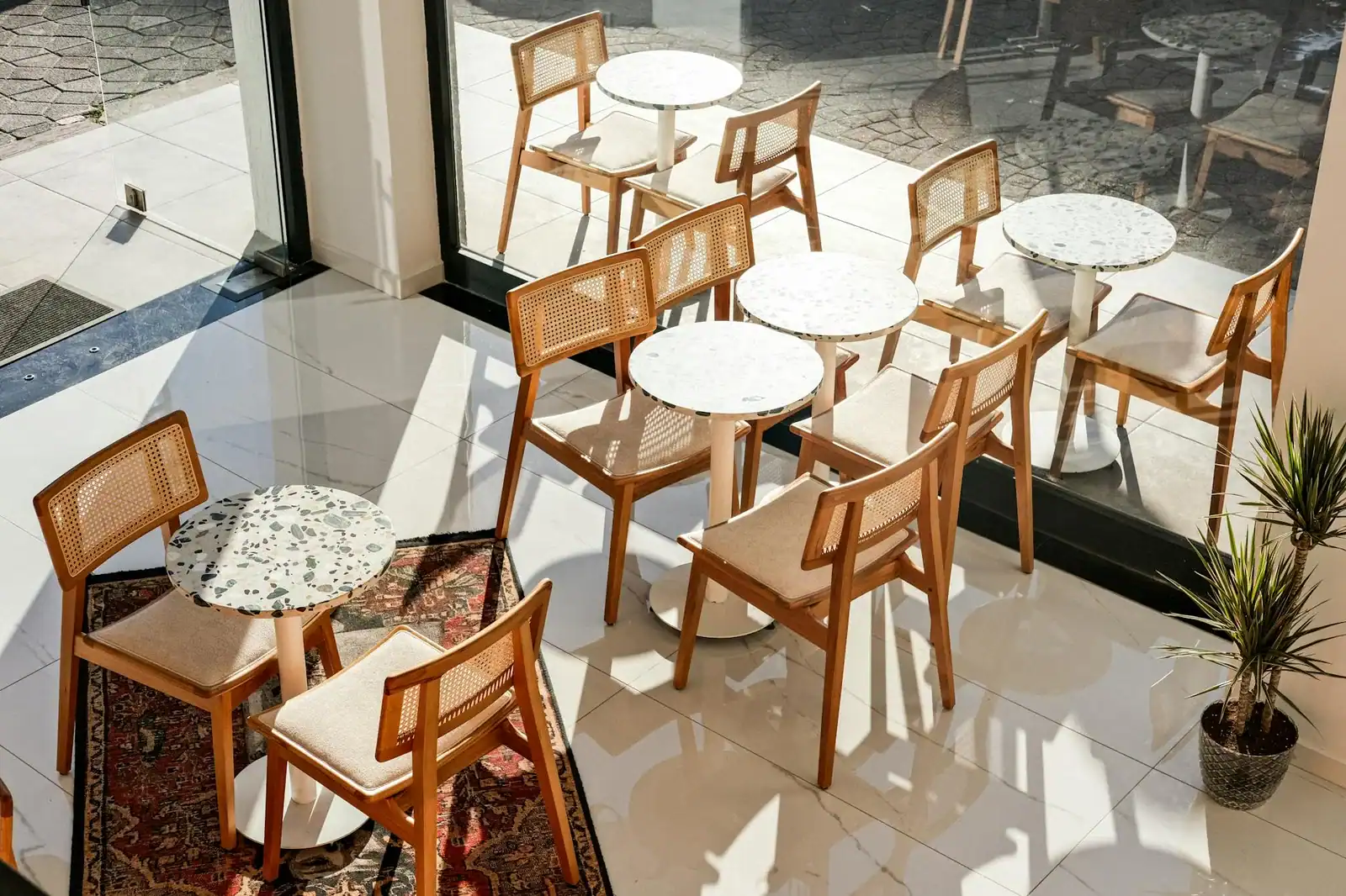 Bright cafe interior featuring wooden chairs and tables by large windows.