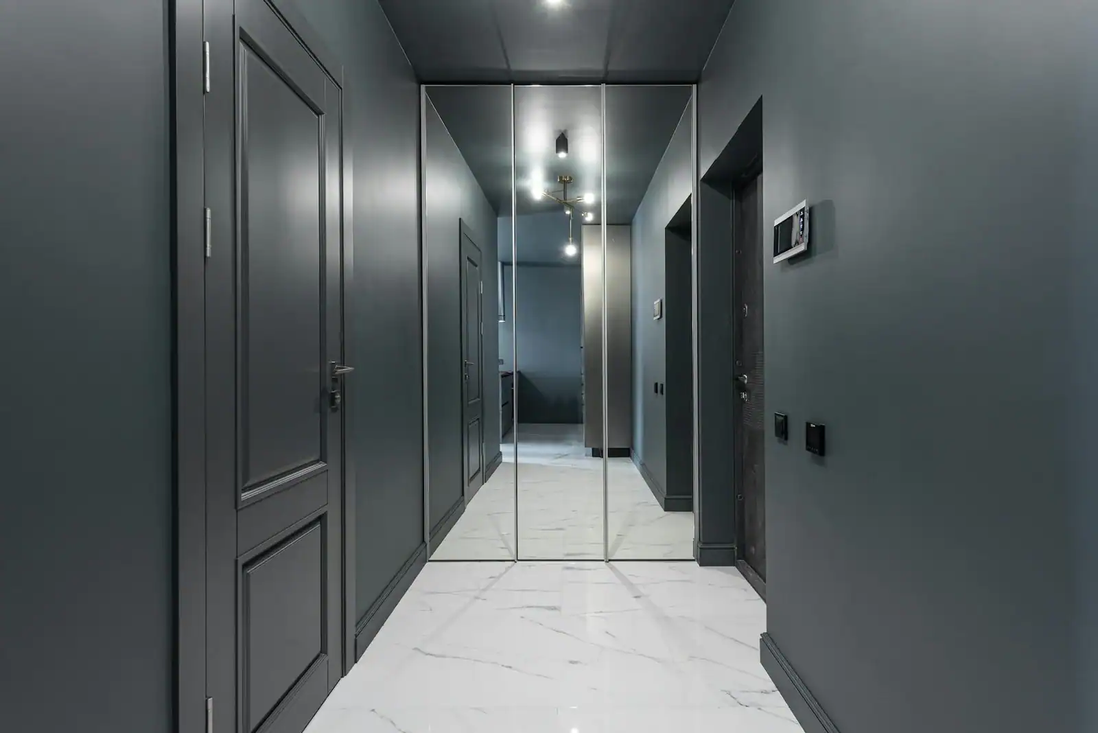 Interior of empty hallway at entrance of modern flat with shining lamps hanging on ceiling and mirror